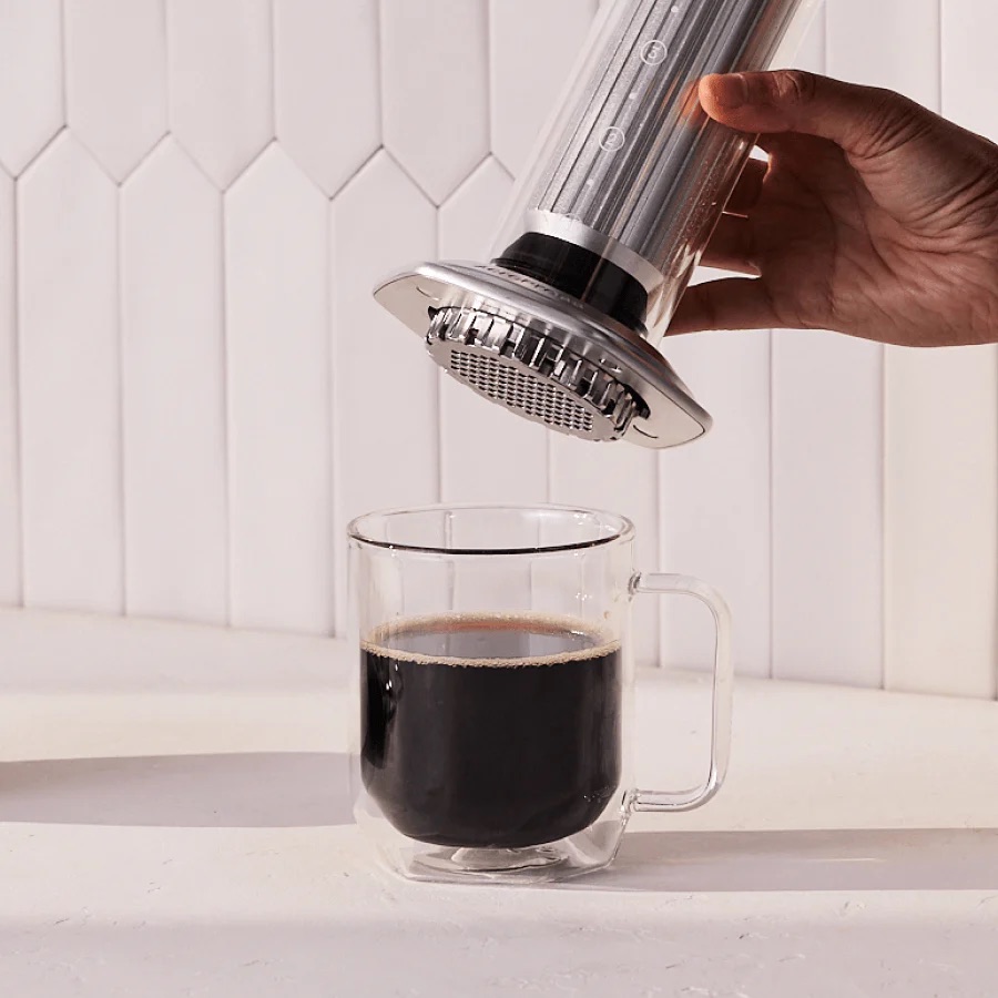 Hand pressing an AeroPress Premium plunger, brewing coffee into a glass mug