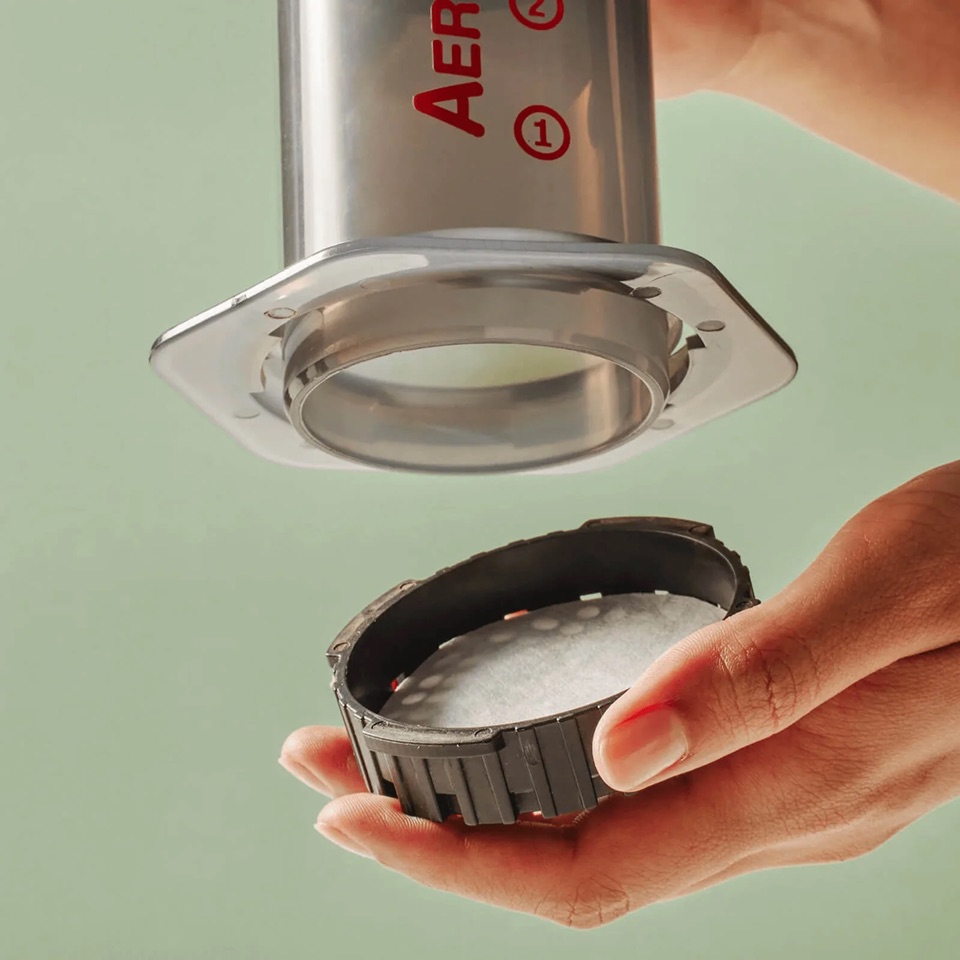 Close-up of hands placing a paper micro-filter into the AeroPress filter cap