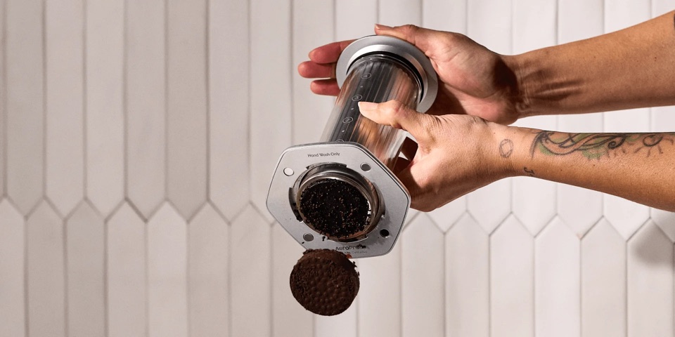 Close-up of hands removing the compact coffee puck from an AeroPress